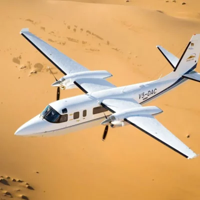 a small plane flying over a sandy area.